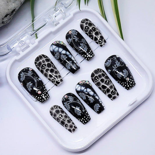 A set of black and white press on nails with a design of flowers and dots, in a white tray on a white background.