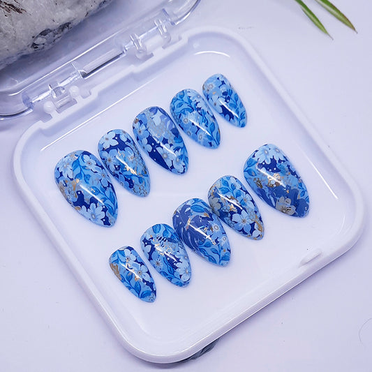 Set of blue floral nail designs in a clear plastic case on a light background