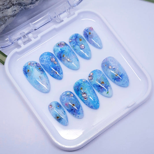 set of blue floral nail designs with some 3d elements displayed in a white case.