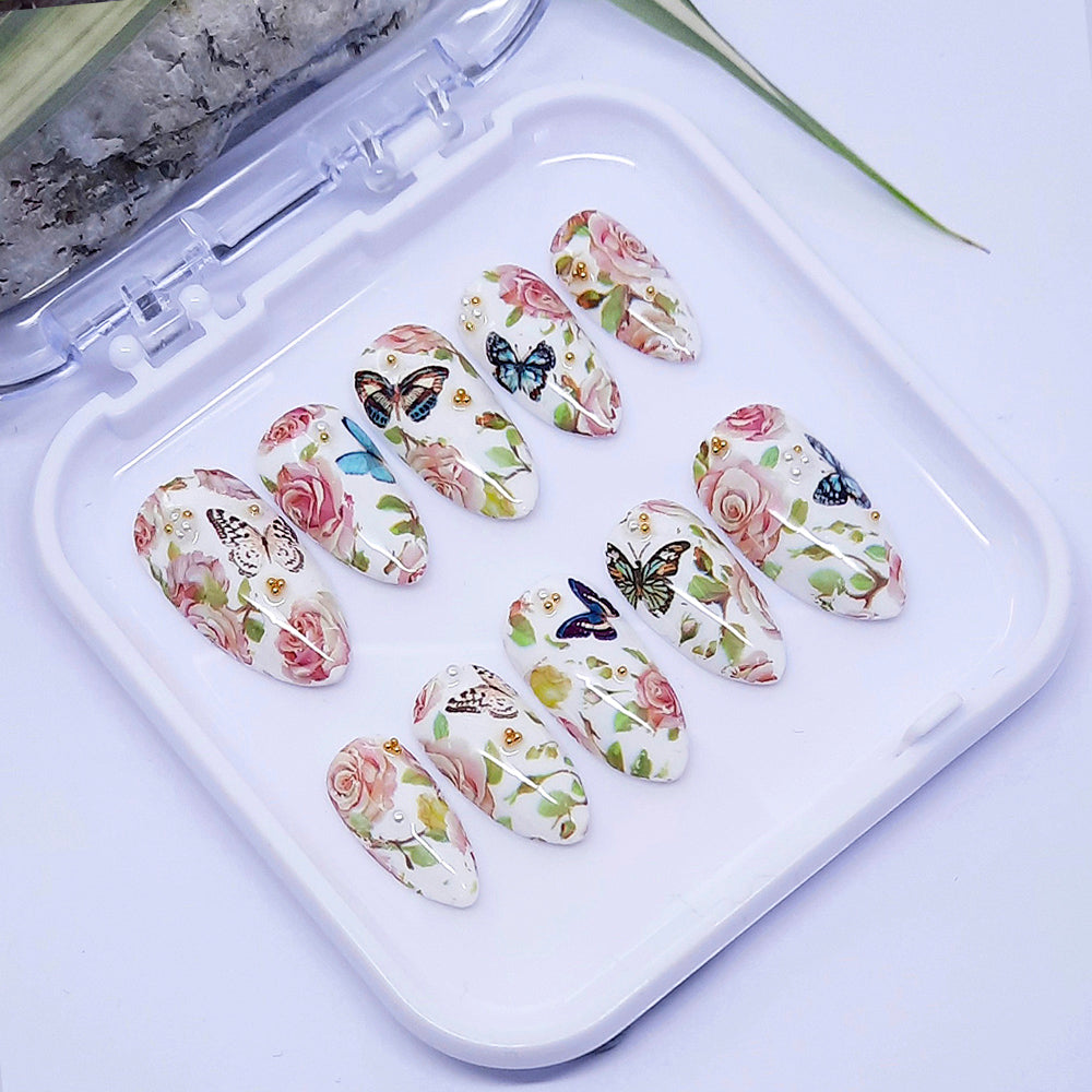A set of white press on nails with a design of roses and butterflies, displayed in a white case.