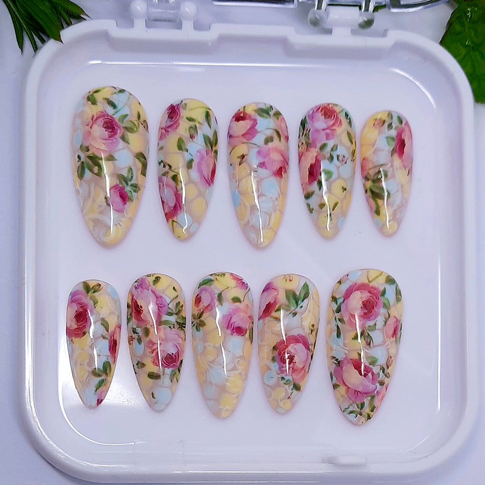 beautiful hand made almond press on nails with a design of pastel blue and yellow, with pink roses, leaves, and subtle white vines