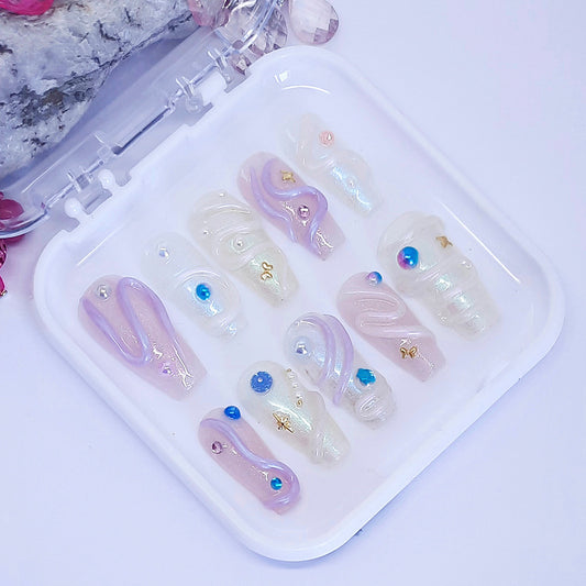 Set of decorative false nails with gemstones on a white tray.