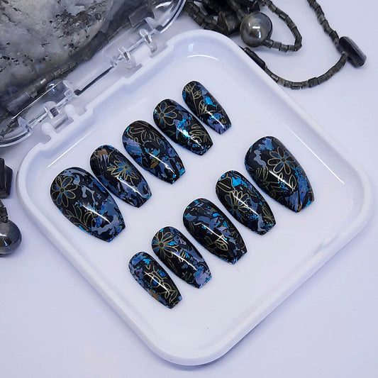 A gorgeous funky set of press on nails, in black with an abstract floral design, with added splashes of blue and grey.