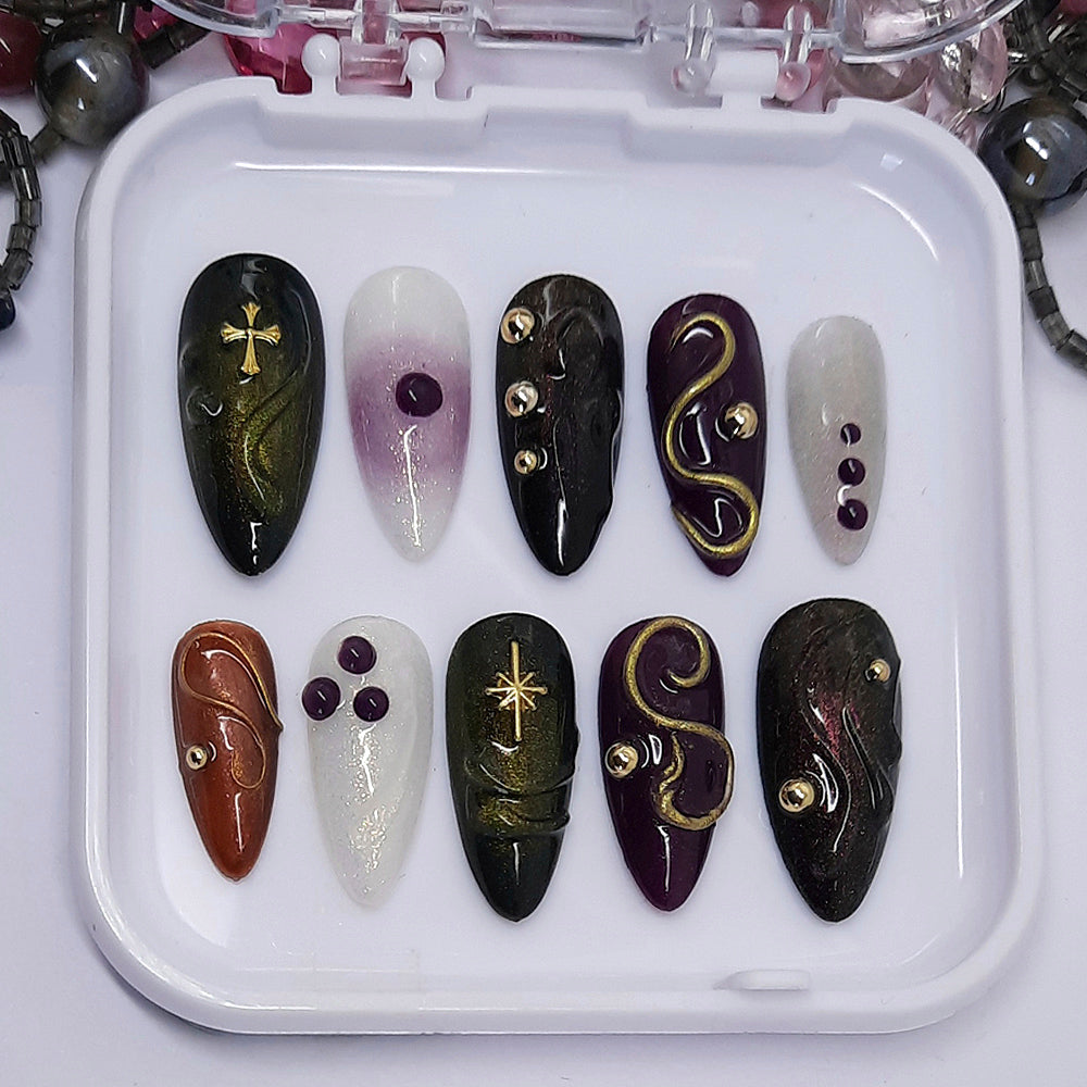 A stunning set of press on nails. In a mix of colours, with some 3d swirls and blobs, and decorated with gold studs, a gold cross, and gold star.