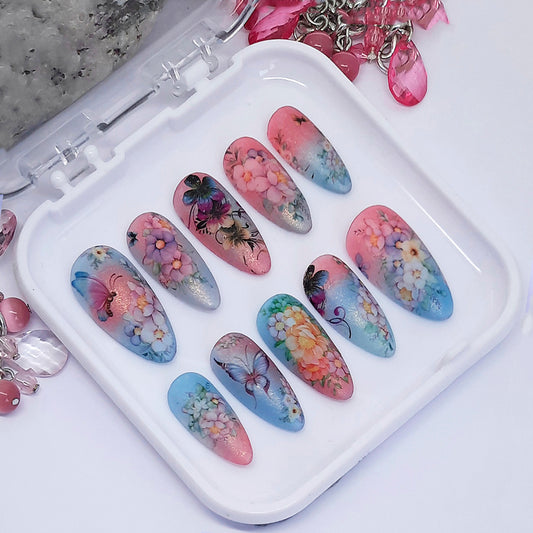 Decorative nail art on press-on nails with floral and butterfly designs, displayed on a white tray.