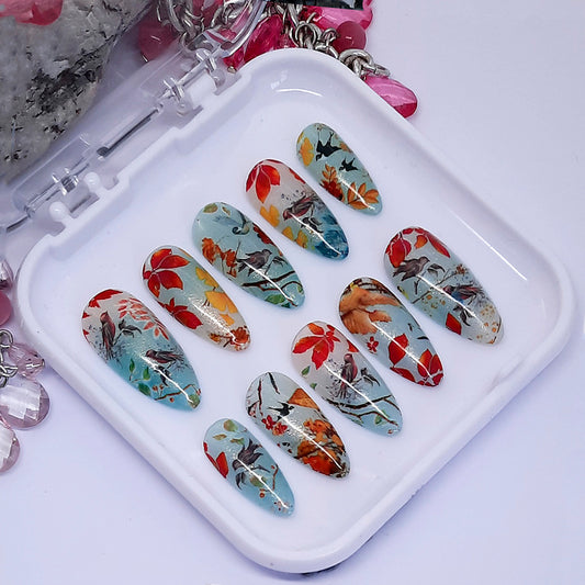 A set of nails with an Autumn themed design, including leaves and birds. Displayed in a white case.