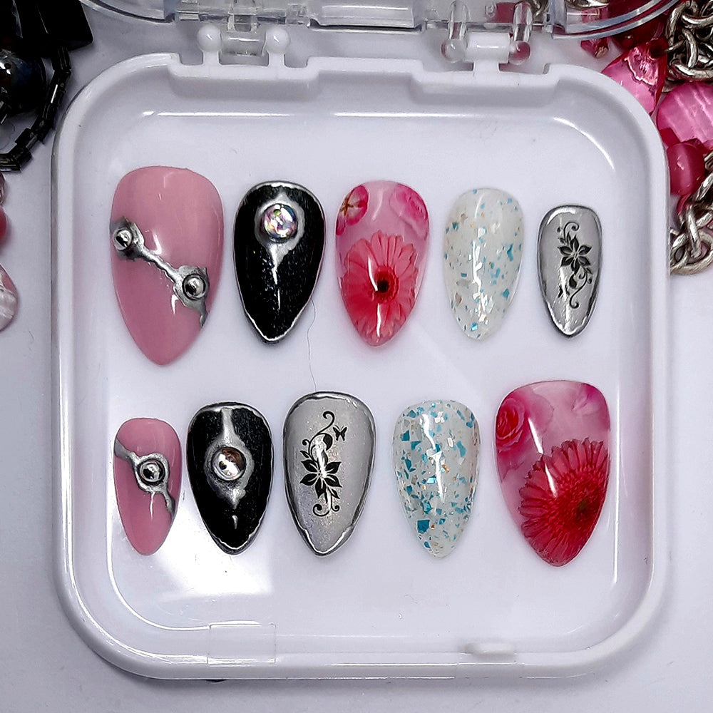 Beautiful press on nails in pink, glittery black, pink jelly, and a sheer sparkly gold; decorated with flowers, silver chrome, silver studs, bubble gems, and glitter. Finished in gloss top coat.
