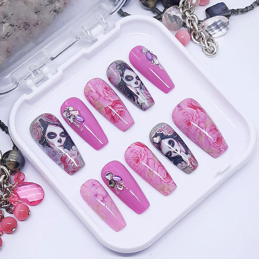 A set of pink and grey press on nails with a floral and faces design and some 3d nail art, displayed in a case on a white background.