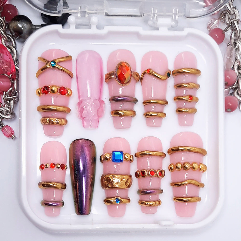 Set of pink and gold nail art designs in a clear case with jewelry items around.