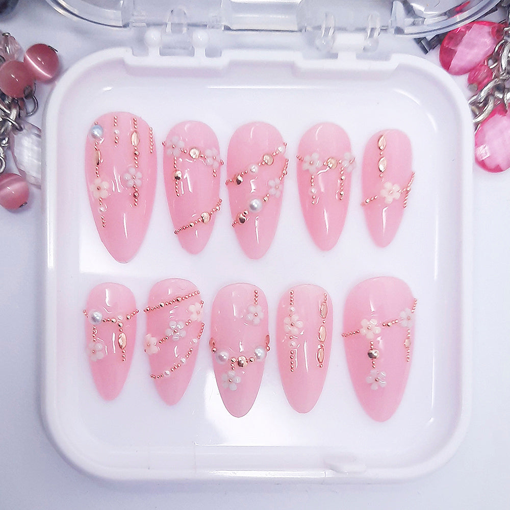 A set of pink press on nails with a 3d design resembling daisy chains Displayed in a white tray on a white background.