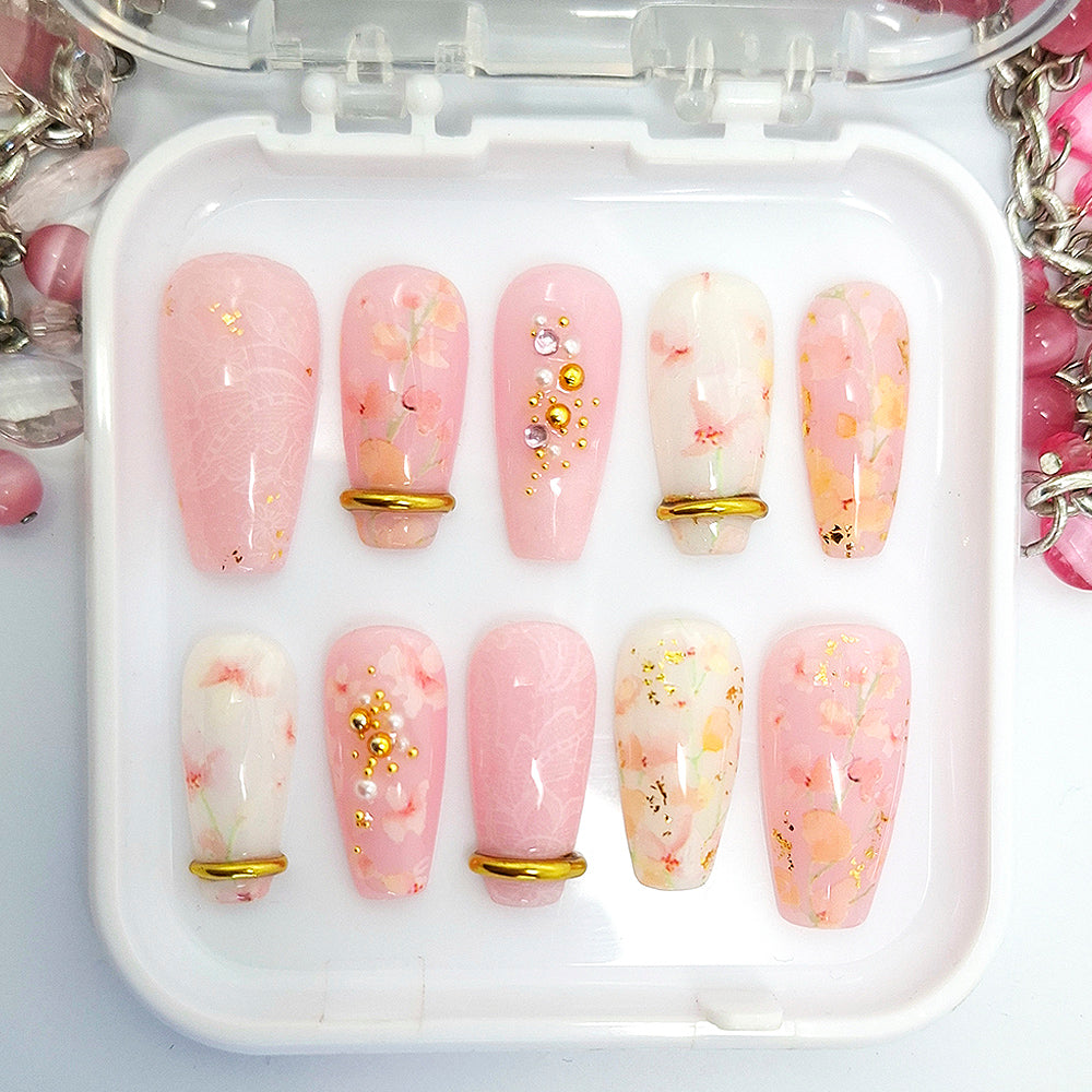 Set of pink and white press on nails with floral and lace design with gold chrome bangles and 3d nail art. Displayed in a white tray on a white background.