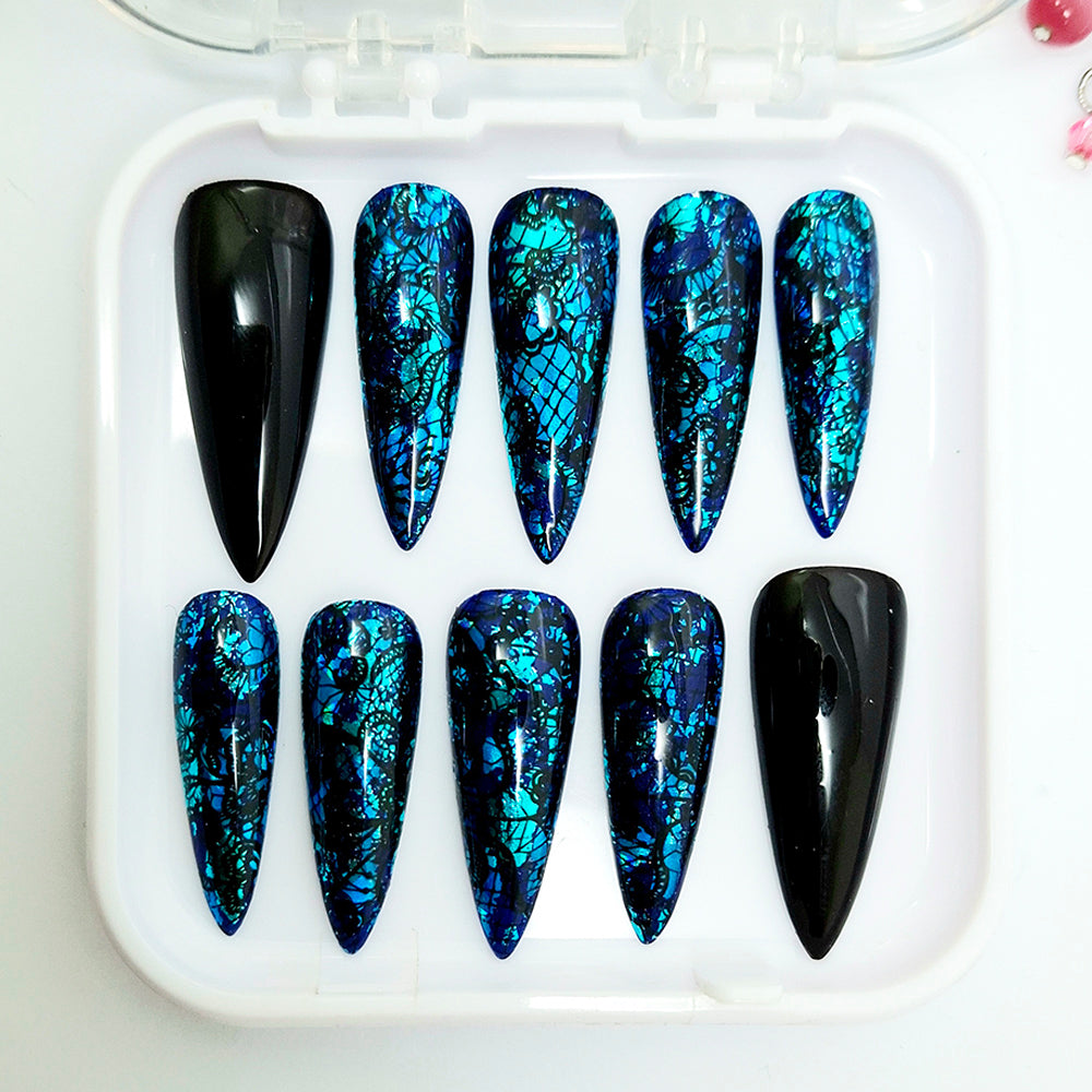 A set of ten stiletto-shaped press-on nails displayed in a clear plastic tray. The nails feature a mix of solid glossy black and a blue and black abstract web-like pattern, set against a clean white background.