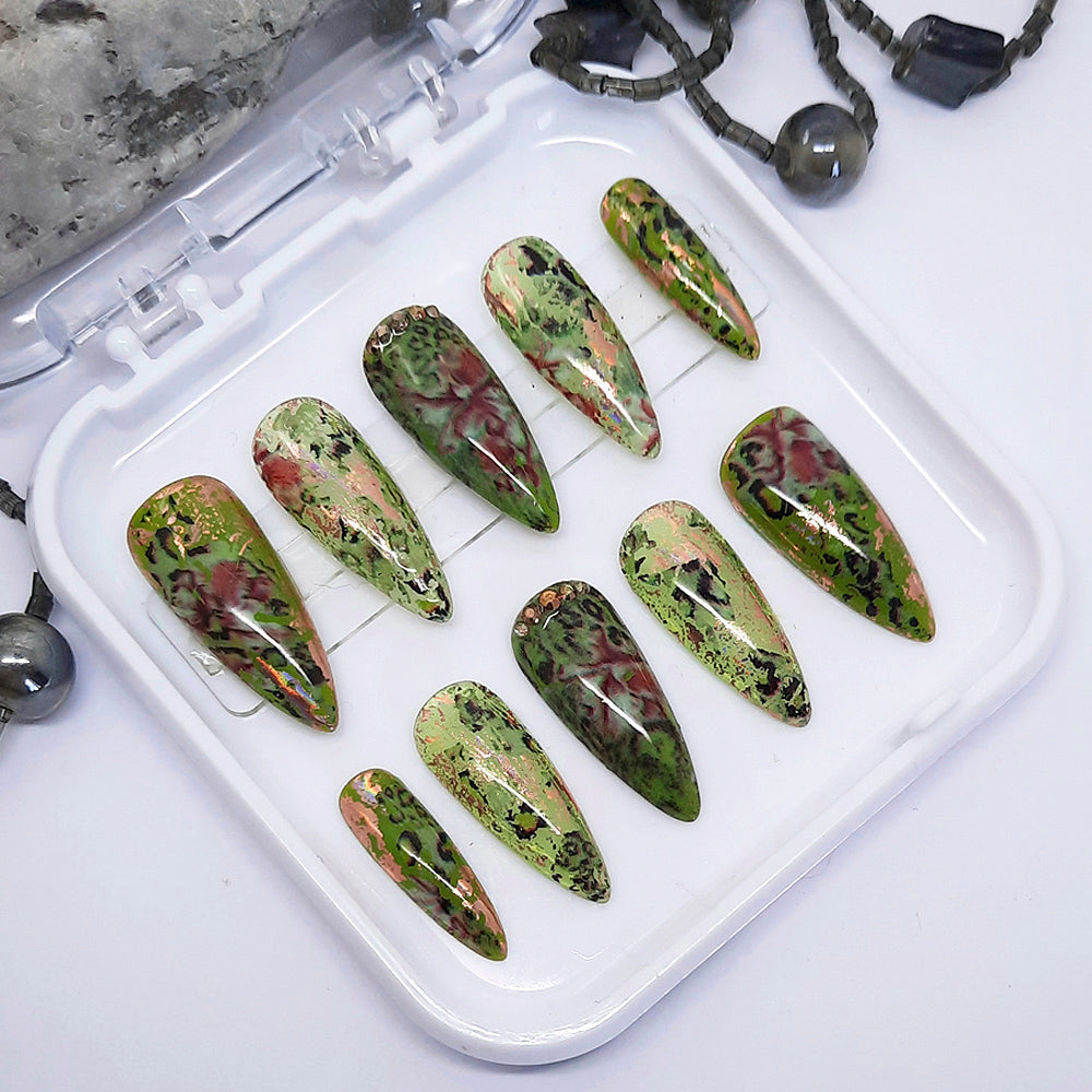 Set of green and red marbled nail art designs on a white tray.