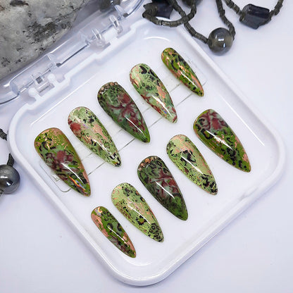 Set of green and red marbled nail art designs on a white tray.