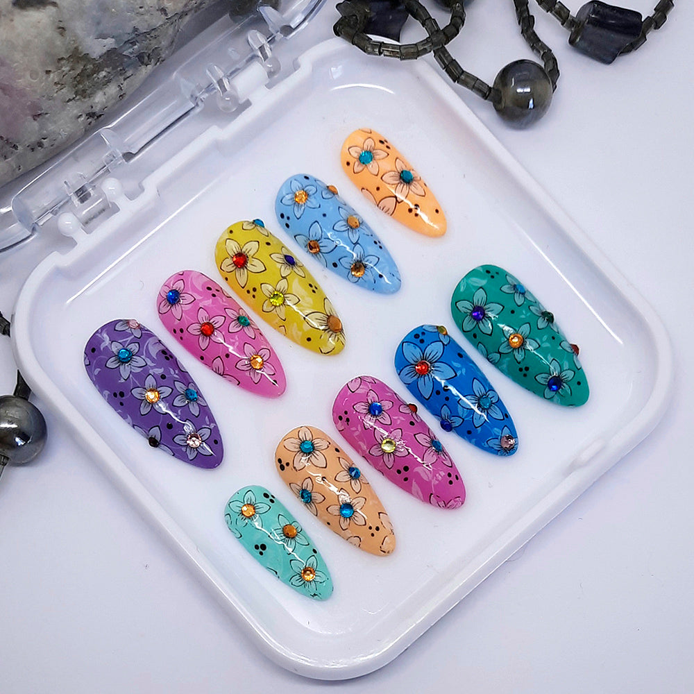 Gorgeous press on nails with each nail a different colour, flowers with a coloured gem at the centre, and finished with a glossy top coat.