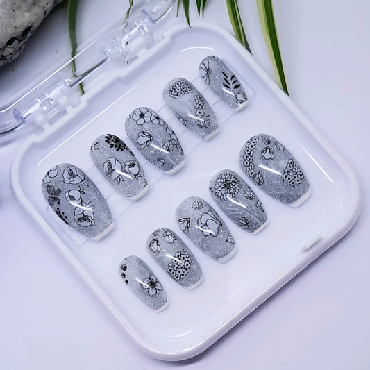 Set of gray nail art designs in a clear plastic case on a light background
