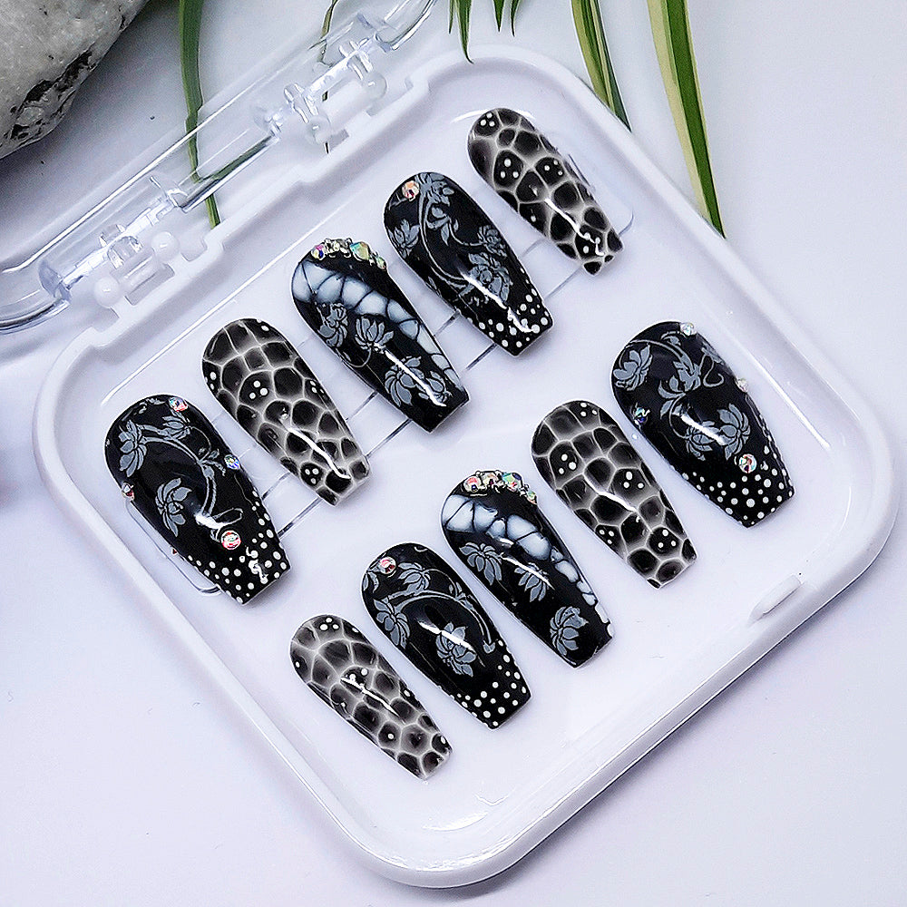 A set of black and white press on nails with a design of flowers and dots, in a white tray on a white background.