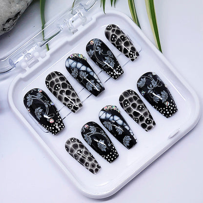 A set of black and white press on nails with a design of flowers and dots, in a white tray on a white background.