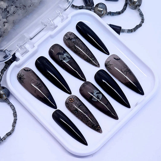 A set of press on nails in solid and sheer black gel polish with Halloween themed designs incluing spider webs.