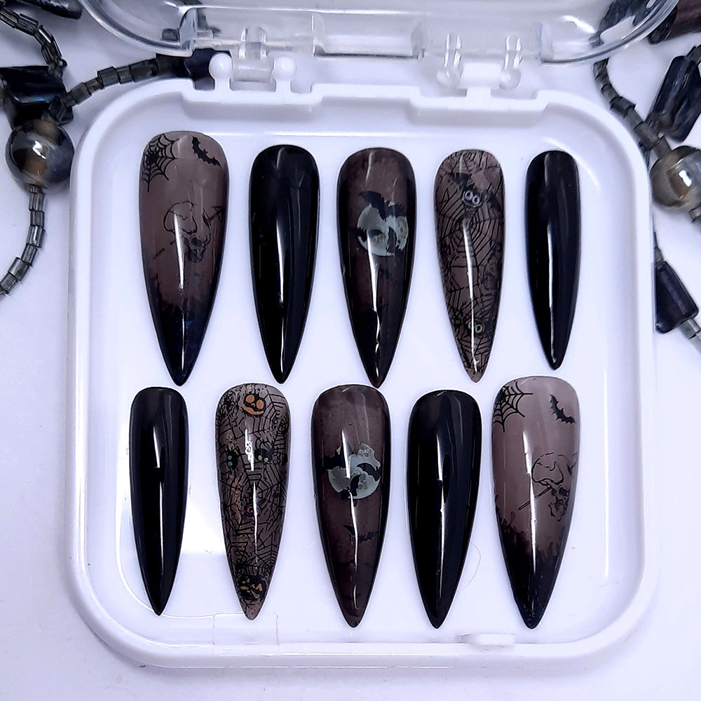 A set of press on nails in solid and sheer black gel polish with Halloween themed designs incluing spider webs.