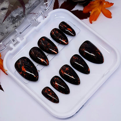 Set of black glossy hand made false nails with flecks of gold.