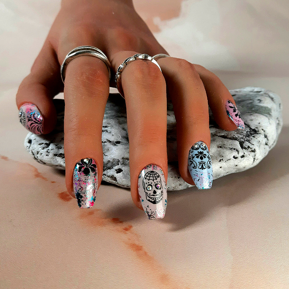 Hand made reusable press on nails in fawn, blue and pink, with coloured foil flecks, skull decals, and crystals.