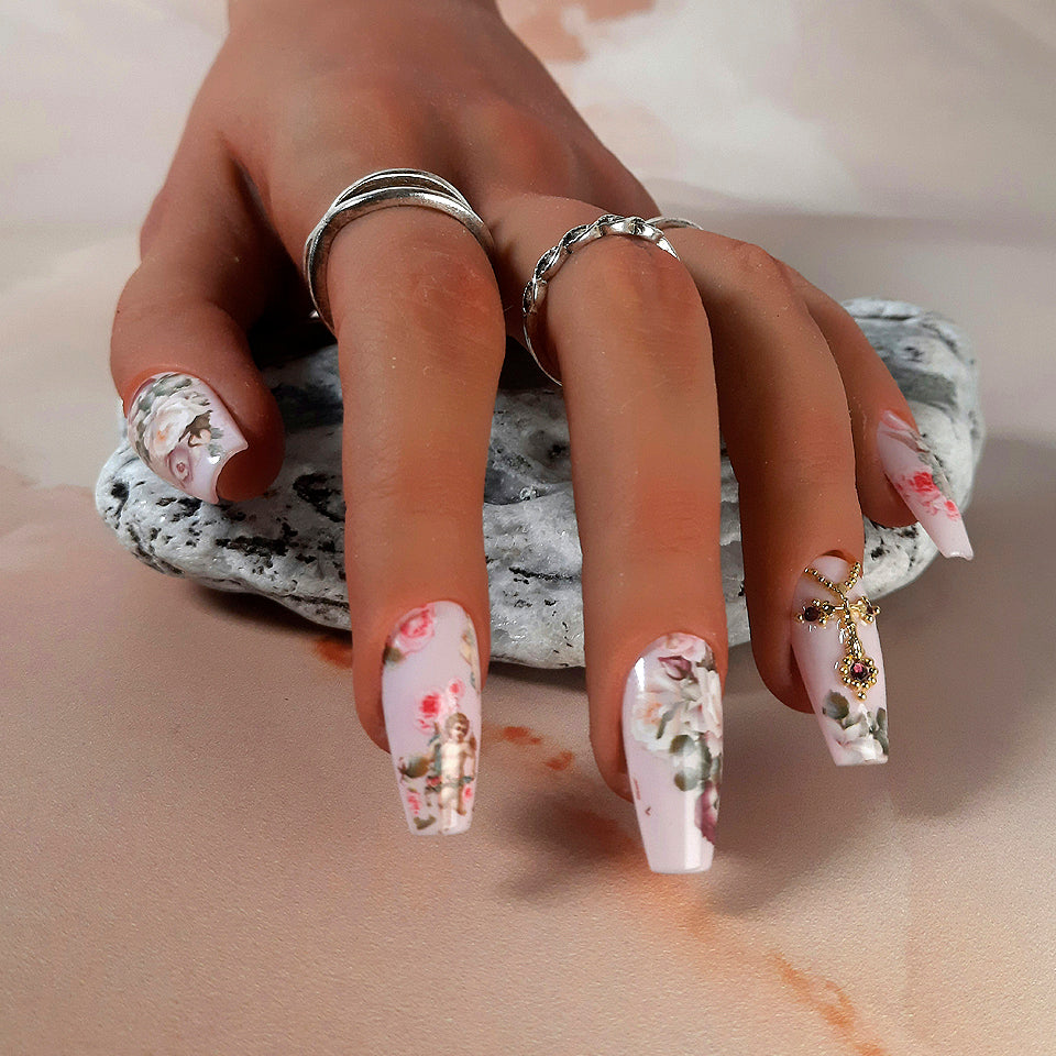 Pale pink hand made press on nails, with a renaissance theme of roses, angels and cupids/cherubs, with an accent nail of a gold cross and gems.