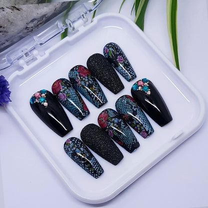 Set of black, snakeskin and floral nail designs on a white tray with a white background