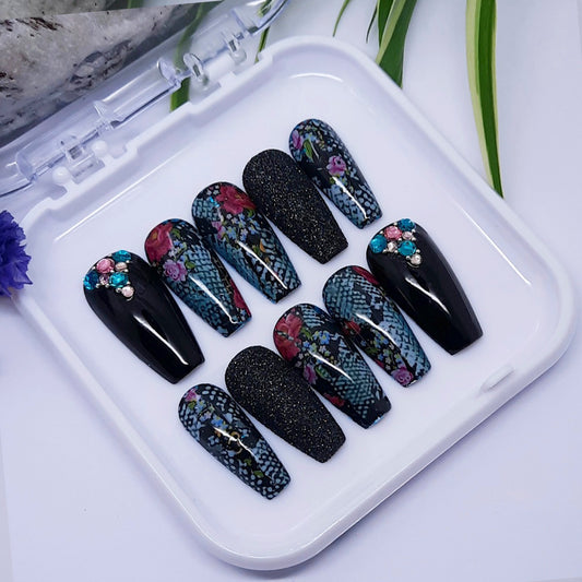 Set of black, snakeskin and floral nail designs on a white tray with a white background