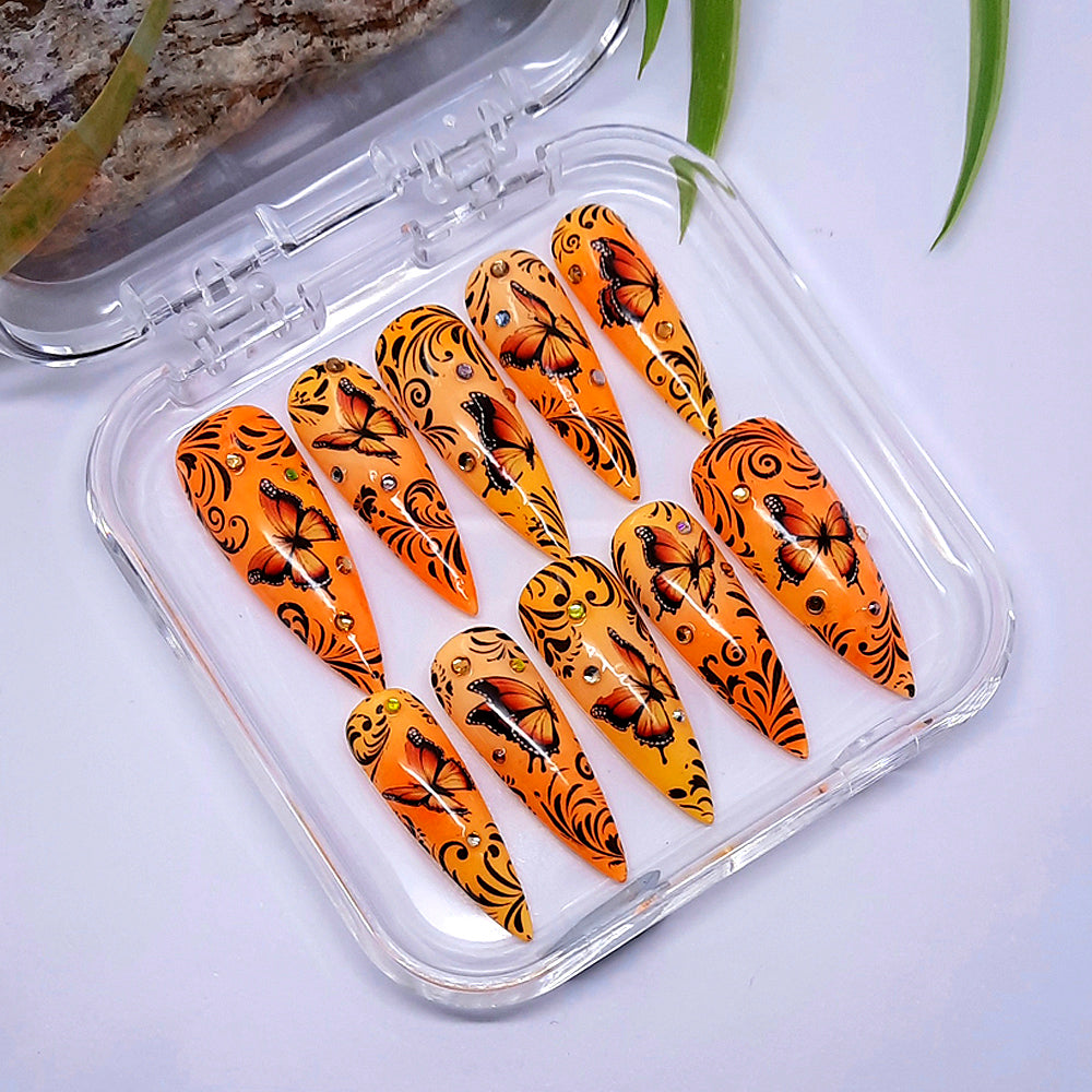 hand made long stiletto press on nails in an orange and yellow ombre, with orange butterflies, black vines and gems.