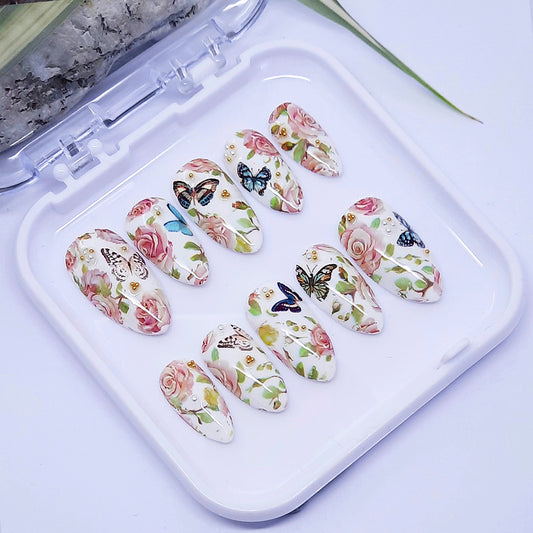 A set of white press on nails with a design of roses and butterflies, displayed in a white case.