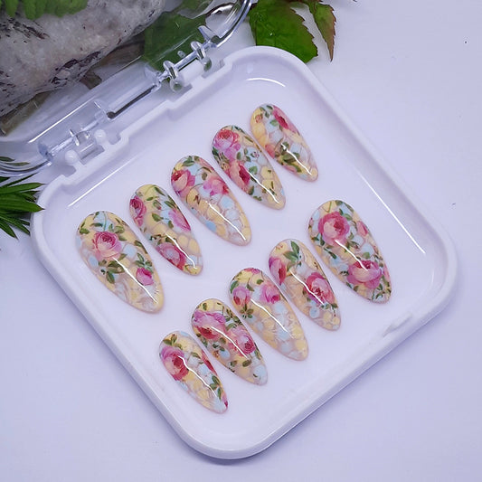 beautiful hand made almond press on nails with a design of pastel blue and yellow, with pink roses, leaves, and subtle white vines