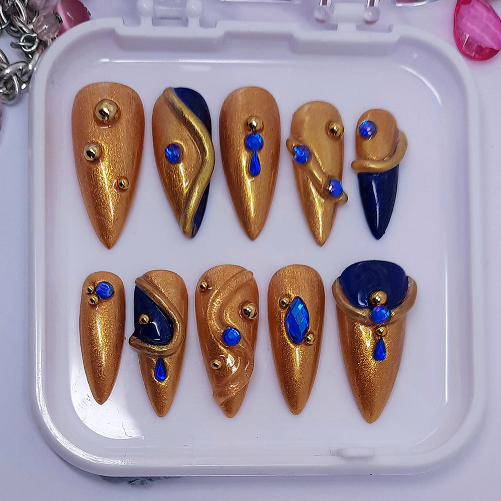 gold hand made press on nails with dark blue accents, blue gems, 3d swirls, and gold studs