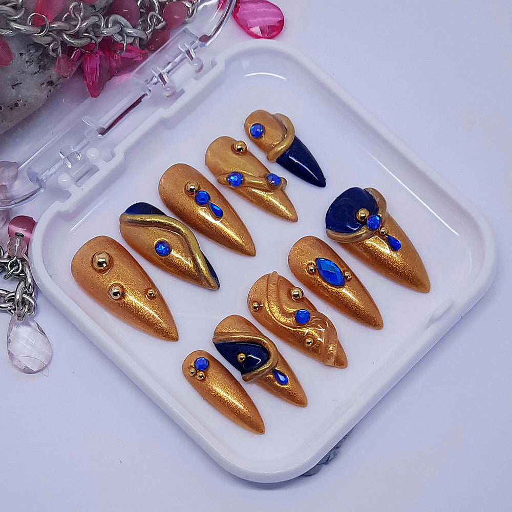 gold hand made press on nails with dark blue accents, blue gems, 3d swirls, and gold studs