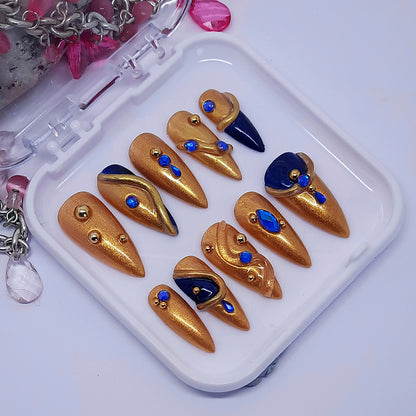 gold hand made press on nails with dark blue accents, blue gems, 3d swirls, and gold studs