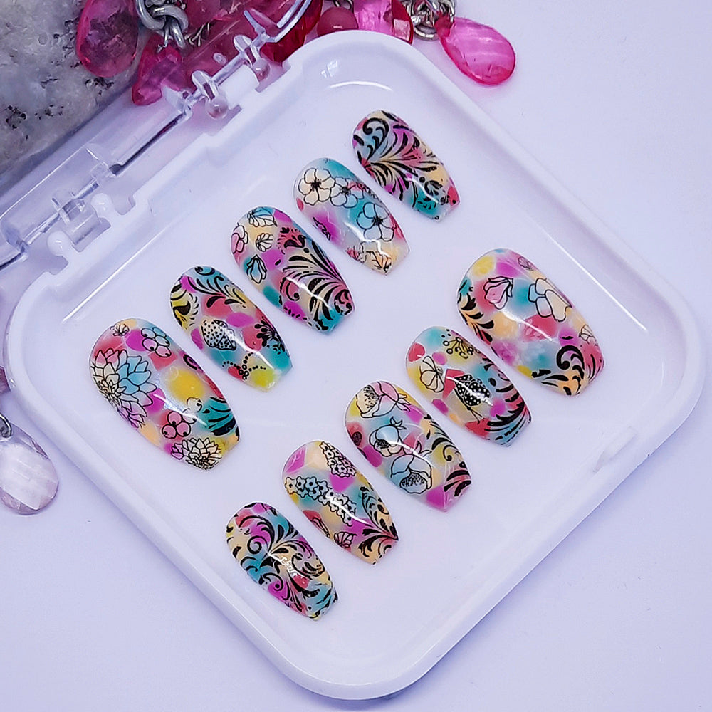 A set of colourful press on nails with an abstract floral design displayed in a white tray on a white background.