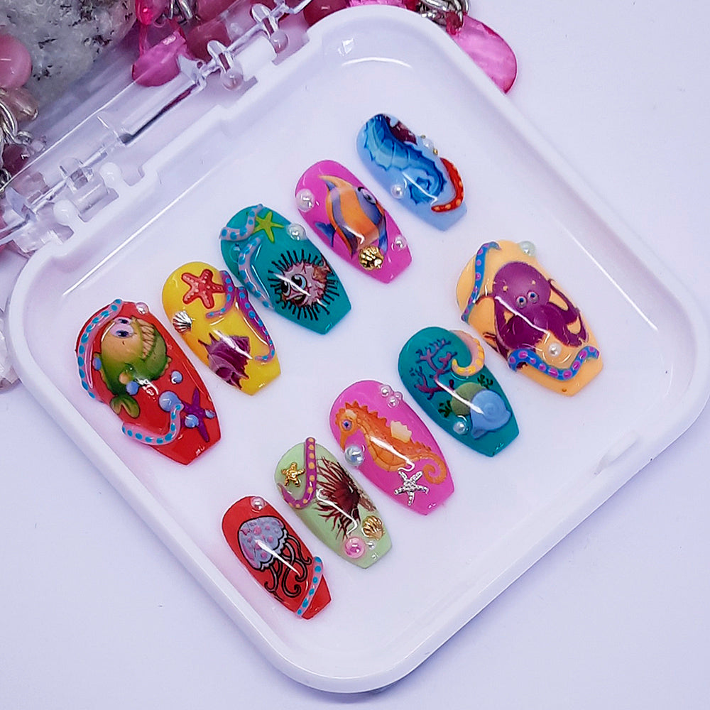 A set of colourful press on nails featuring a sea-life design including fish, starfish and octopus and some 3d nail art. Displayed in a white case on a white background.