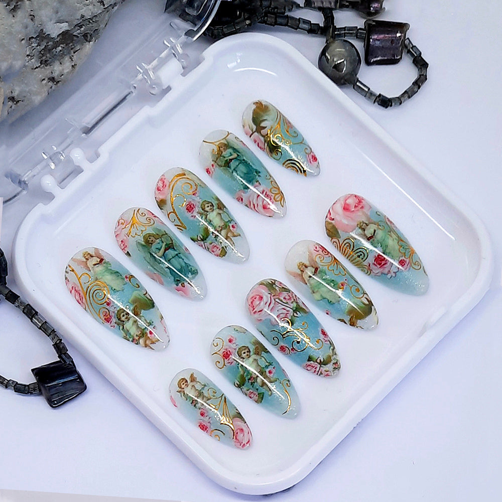 A set of nails with a design of roses, angels and cherubs displayed in a white case.