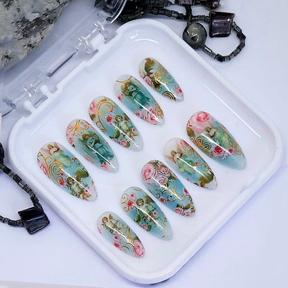 A set of nails with a design of roses, angels and cherubs displayed in a white case.
