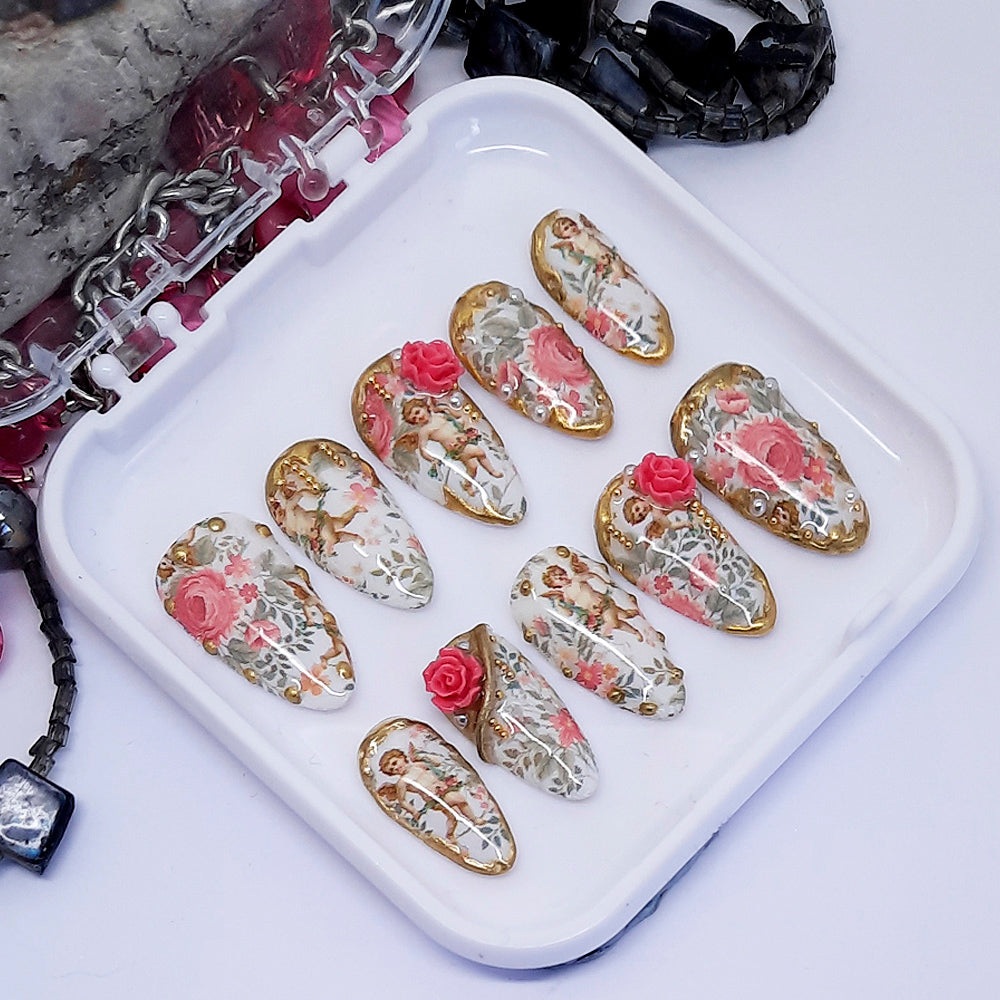 Decorative nail art designs with cherubs and roses on a white tray with a white background