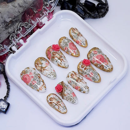 Decorative nail art designs with cherubs and roses on a white tray with a white background
