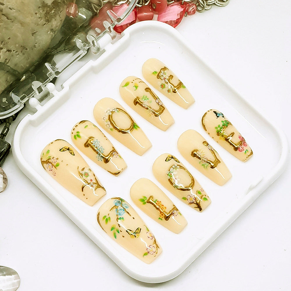 Set of pastel yellow nail extensions with gold accents on a white tray.