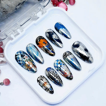Set of silver metallic press on nails with nail art designs on a white tray with decorative elements.