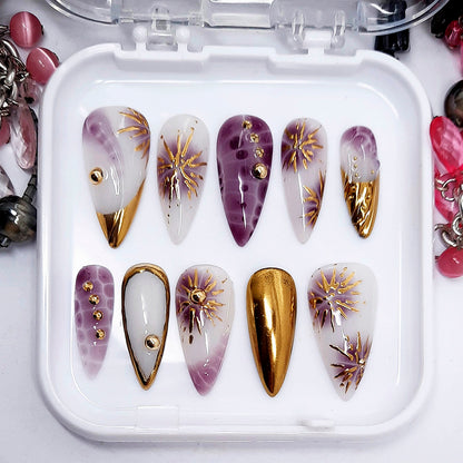 Set of nail art designs in a white case with purple, gold, and white colors.