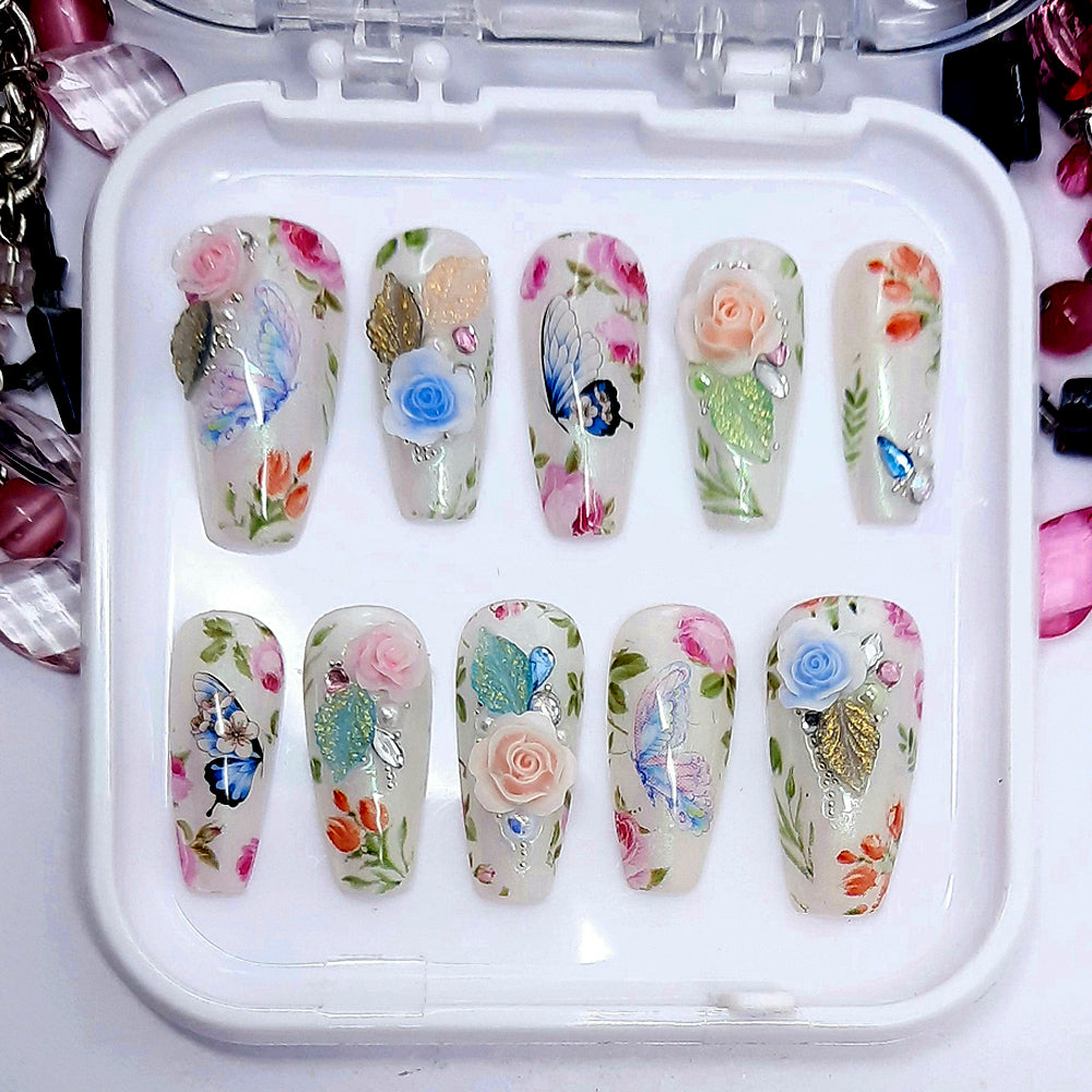 Beautifully romantic press on nails in milky white with subtle chrome; decorated with flowers, butterflies, and some beautiful 3d roses, leaves, pearls, gems and beads. Finished in gloss top coat.