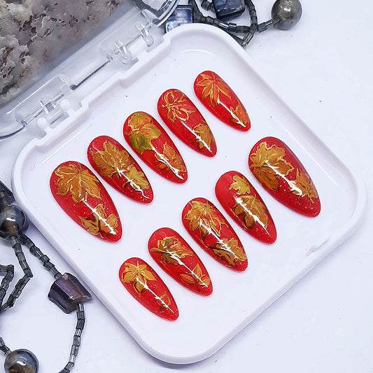 Red nail art designs with gold leaf patterns on a white tray.