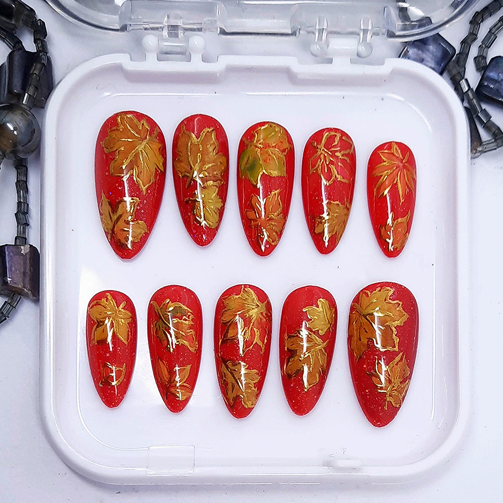 Red nail art designs with gold leaf patterns in a white container.