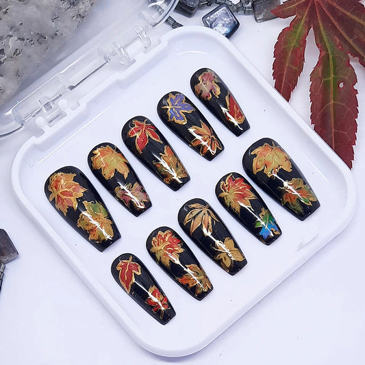 Nail art display with black nails featuring colorful leaf designs on a white tray.