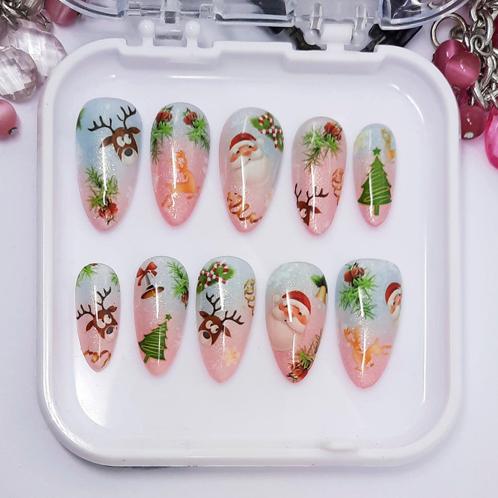 A set of pink and blue ombre press on nails with a cute Christmas themed design, displayed in a white tray on a white background.