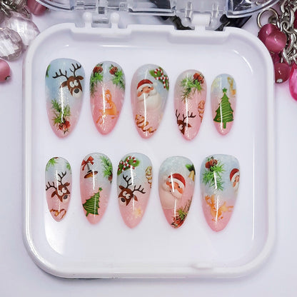 A set of pink and blue ombre press on nails with a cute Christmas themed design, displayed in a white tray on a white background.